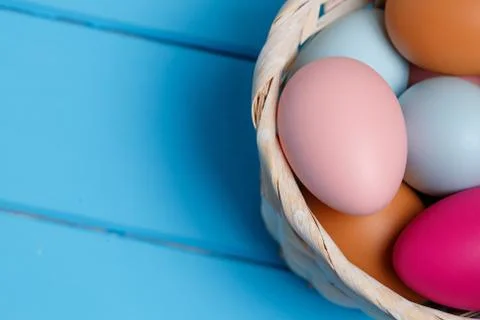 Colorful easter egg in the basket on blue wood background with space. Stock Photos