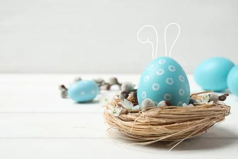 Colorful Easter egg with cute bunny ears in decorative nest on white wooden t Stock Photos