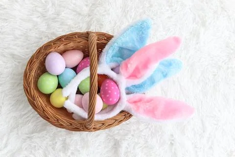 Colorful Easter eggs and bunny rabbit ears headband in wicker basket on flu.. Stock Photos