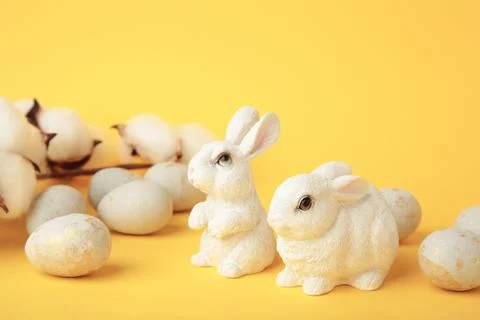 Colorful easter eggs and ceramic bunny figurines on yellow background Stock Photos