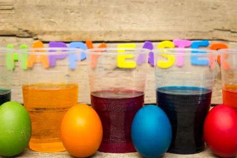 Colorful easter eggs and cups of dye in front of a wooden background Stockfoto's
