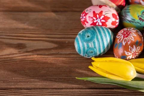 Colorful Easter eggs arranged on brown boards with a few yellow tulips. Stock-Fotos