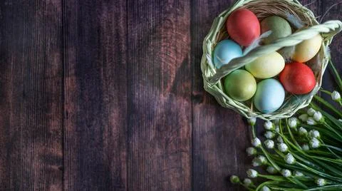 Colorful Easter eggs in a basket on the background of a wooden table, next to Stock Photos