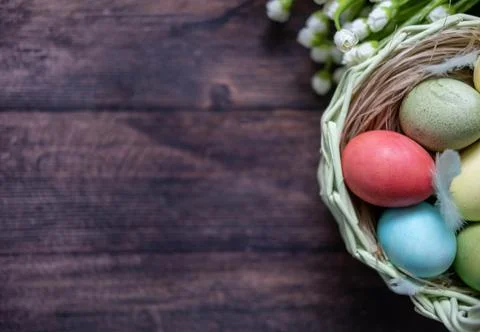 Colorful Easter eggs in a basket on the background of a wooden table, next to Stock Photos