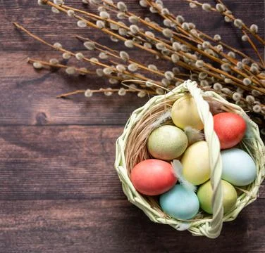 Colorful Easter eggs in a basket on the background of a wooden table, next to Stock Photos