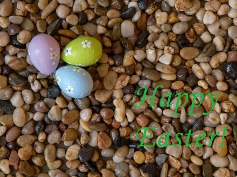 Colorful Easter eggs on bed of beach pebbles with Happy Easter greeting Stock Photos