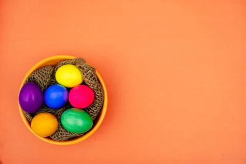Colorful Easter Eggs in Bowl with Rustic Thread Decor isolated On orange Stock Photos