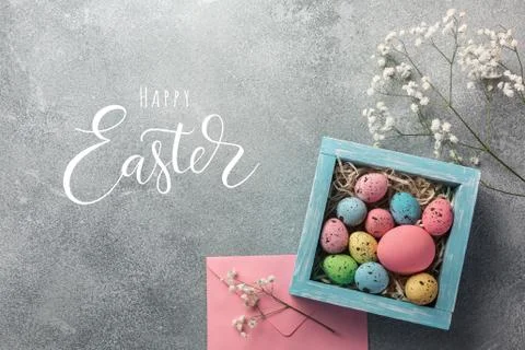 Colorful easter eggs in box and flowers on table. Top view with copy space. Stock Photos