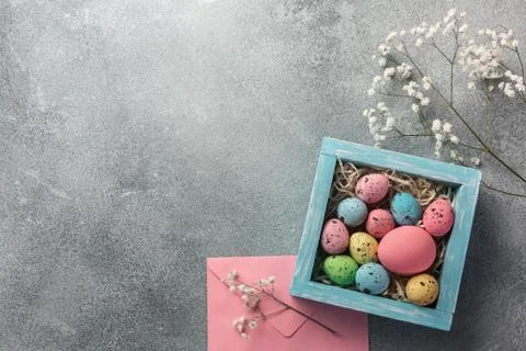 Colorful easter eggs in box and flowers on table. Top view with copy space. Stock Photos