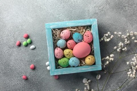 Colorful easter eggs in box and flowers on table. Top view with copy space. Stock Photos