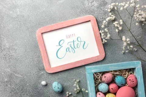 Colorful easter eggs in box and flowers on table. Top view with copy space. Stock Photos