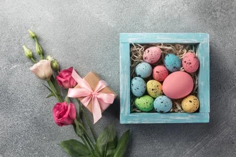 Colorful easter eggs in box and gift, flowers on table. Top view with copy sp Foto stock
