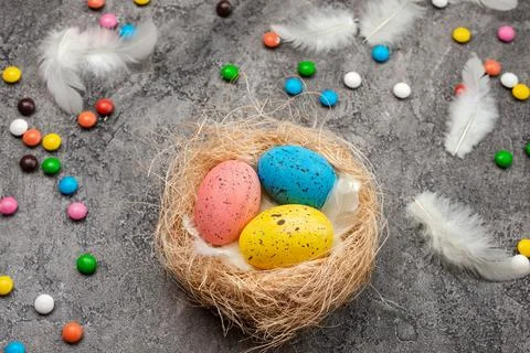 Colorful easter eggs with feathers and sweets in nest on dark background. Stock Photos