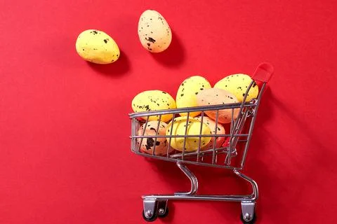 Colorful Easter eggs fly out of the shopping cart on the red background. East Stock Photos