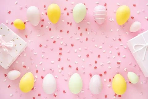 Colorful Easter eggs frame with bunny ears sugar sprinkle and gift box on pink Stock Photos