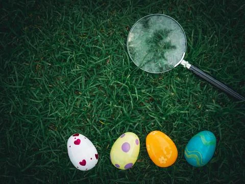 Colorful Easter eggs on green grass with magnifying glass, Easter egg hunter Stock Photos