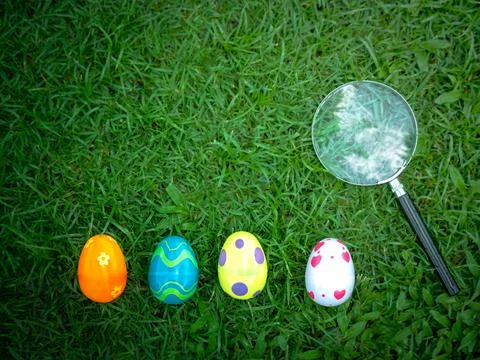 Colorful Easter eggs on green grass with magnifying glass, Easter egg hunter Stock Photos