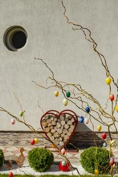 Colorful easter eggs hanging on tree branches in front of a gray house yard Stock Photos