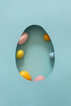 Colorful Easter eggs inside egg shaped cutout  against pastel blue background Stock Photos