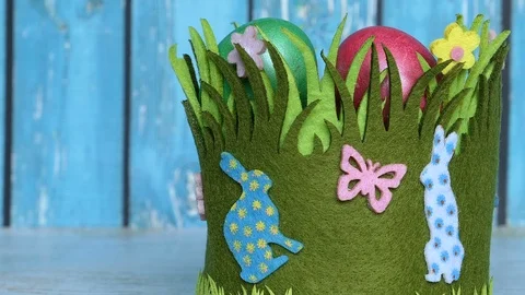 Colorful Easter Eggs Lying In A Grass Basket With Easter Rabbits On A Blue Woode Vídeos de archivo 126589380