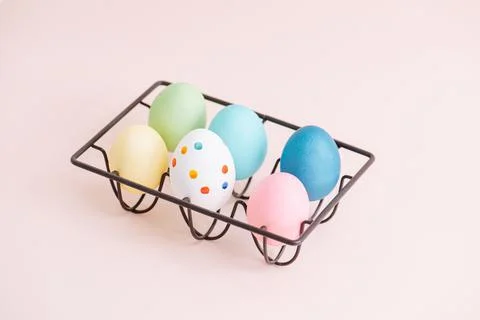 Colorful easter eggs on a metal egg holder over pink surface Stock Photos