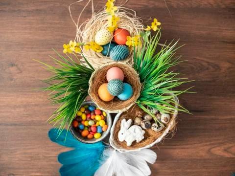 Colorful Easter eggs in nest, feathers and spring flowers on wooden table. Ea Stock Photos
