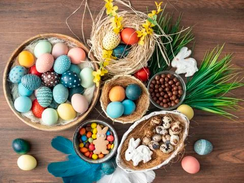 Colorful Easter eggs in nest, feathers and spring flowers on wooden table. Ea Stock Photos