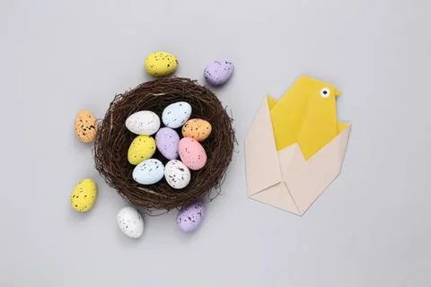 Colorful easter eggs in a nest with a paper chick on a gray background Stock Photos