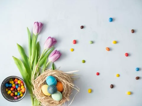 Colorful Easter eggs in nest, spring flower, tulips and candies on bright bac Foto stock