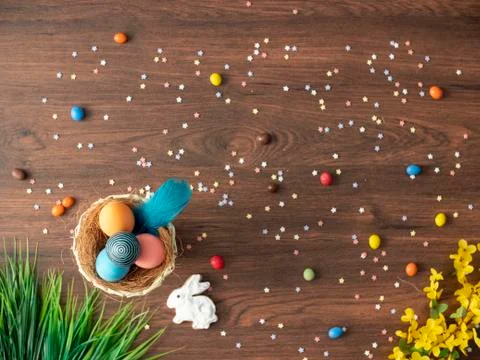 Colorful Easter eggs in nest, spring flowers and candy on wooden table. Easte Stock Photos