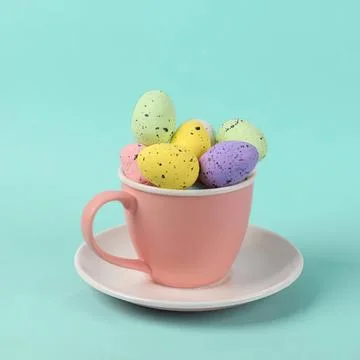 Colorful easter eggs in pink cup with saucer on blue background Stock Photos