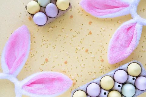 Colorful Easter eggs with rabbit ears and confetti on yellow background. Stock Photos