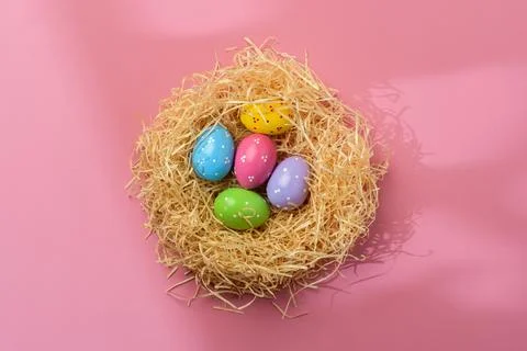 Colorful Easter eggs rest in straw nest on pink background, cheerful spring Stock Photos