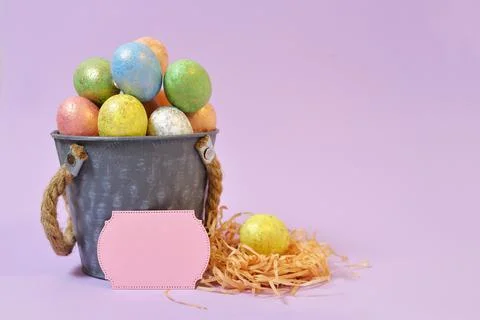 Colorful Easter eggs on a soft purple background in a gray bucket in the styl Stock Photos