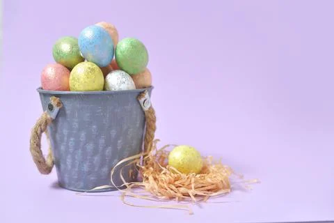 Colorful Easter eggs on a soft purple background in a gray bucket in the styl Stock Photos