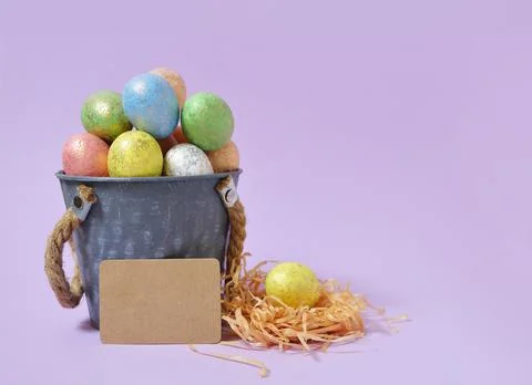 Colorful Easter eggs on a soft purple background in a gray bucket in the styl Stock Photos