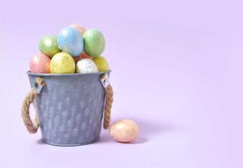 Colorful Easter eggs on a soft purple background in a gray bucket in the styl Stock Photos
