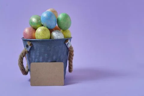 Colorful Easter eggs on a soft purple background in a gray bucket in the styl Stock Photos