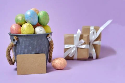Colorful Easter eggs on a soft purple background in a gray bucket in the styl Stock Photos