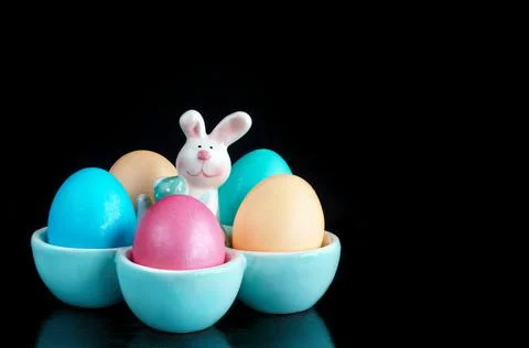 Colorful Easter eggs in a stand with a rabbit on a black background. Selective Stock Photos