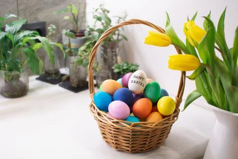 Colorful Easter eggs in wicker basket on table in kitchen interior with tulips 스톡 사진
