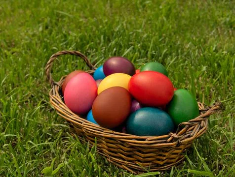 Colorful Easter eggs in a wicker basket standing on the grass Foto stock