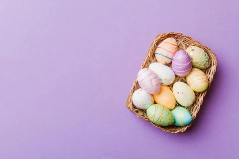 Colorful Easter eggs in wicker basket against colored background, closeup. to 库存照片