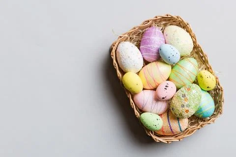 Colorful Easter eggs in wicker basket against colored background, closeup. .. 写真素材