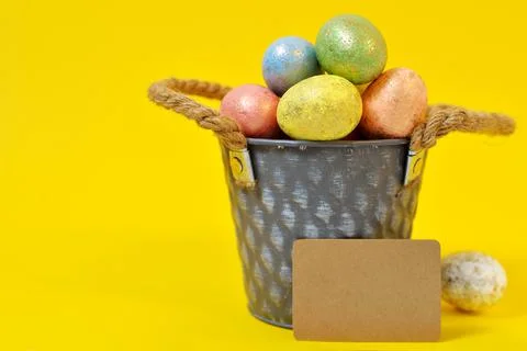 Colorful Easter eggs on a yellow background in a gray bucket in the style of  Stock Photos