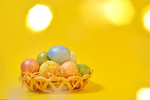 Colorful Easter eggs on a yellow background in a wicker basket in the style o Stock Photos