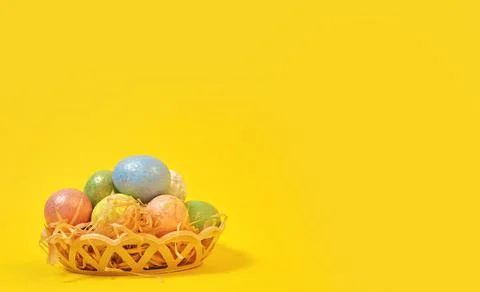 Colorful Easter eggs on a yellow background in a wicker basket in the style o Stock Photos