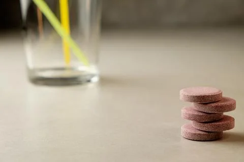 Colorful effervescent tablets rest beside an empty glass on a clean surface Stock Photos