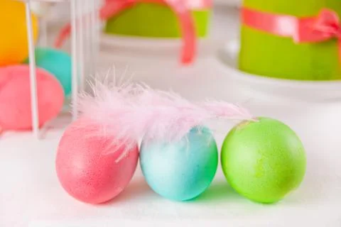 Colorful eggs for Easter day with feather, gift box and small cake on the bac Photos