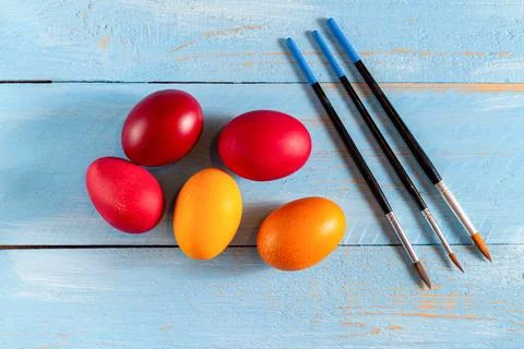 Colorful eggs for Easter with ears of grain and paintbrush on blue wooden bac Stock Photos